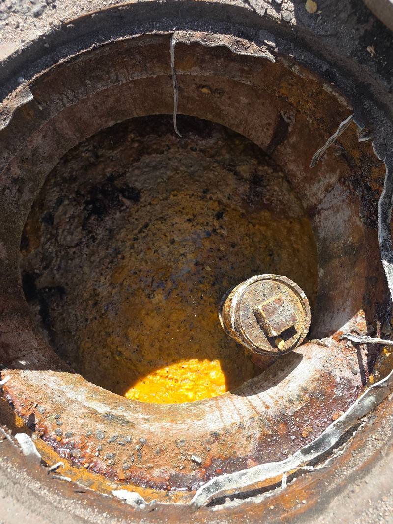Looking into a grease interceptor opening with orange-yellow grease buildup around a brass cleanout cap